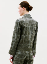 Load image into Gallery viewer, A person with fair skin and brown hair in a bun is seen from behind, wearing the Lesath Jacket in gray with matching pants, standing against a plain light background.
