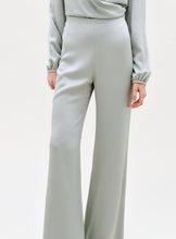 Load image into Gallery viewer, A person wearing the Palermo Pant—high-waisted, light gray wide-leg pants—shown from mid-torso to feet with one hand by their side against a plain background.
