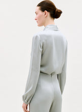 Load image into Gallery viewer, A person with brown hair in a low bun wears the light gray, long-sleeved Tea Blouse and matching high-waisted pants, shown from the back and side against a plain light background.
