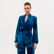 Load image into Gallery viewer, A woman stands against a plain light background, wearing the Tea Blouse in blue velvet with matching high-waisted pants. She looks directly at the camera with a neutral expression.

