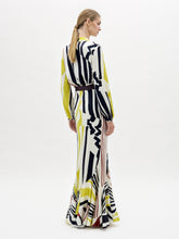 Load image into Gallery viewer, A woman stands wearing the Florina Skirt, a long, flowing piece with vertical and diagonal stripes in black, yellow, and red.
