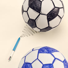 Load image into Gallery viewer, Two soccer balls with a pen on a beige background.
