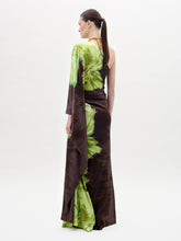 Load image into Gallery viewer, A person models the Afrodita Dress—a one-shoulder, floor-length gown with a green and brown tie-dye print—paired with gold necklaces, against a plain white background.
