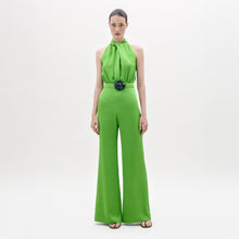 Load image into Gallery viewer, A woman stands facing forward in the Siv Jumpsuit, a bright green halter-neck style with wide-leg pants and a matching belt, paired with black sandals, against a plain white background.
