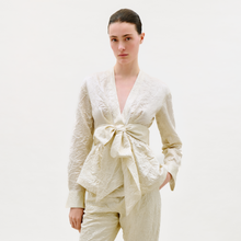 Load image into Gallery viewer, Woman wearing a cream-colored outfit with a tie detail on a white background
