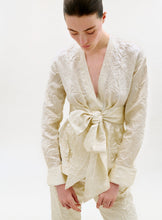 Load image into Gallery viewer, Woman wearing a cream-colored textured outfit with a bow detail on a white background
