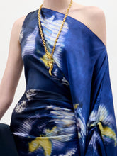 Load image into Gallery viewer, A woman stands against a plain background wearing the Dotty Dress, a one-shoulder blue dress with a yellow and white floral pattern, and holds a black clutch with a fringe strap.
