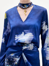 Load image into Gallery viewer, Woman wearing the Lane Blouse, a blue patterned top, paired with a matching skirt and choker necklace, standing against a plain light background.
