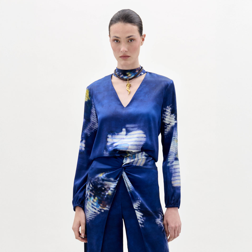 Woman wearing the Lane Blouse, a blue patterned top, paired with a matching skirt and choker necklace, standing against a plain light background.