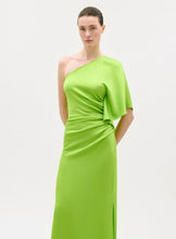 Load image into Gallery viewer, A woman models the Doli Dress, a vivid green one-shoulder maxi crafted from Italian fabric with a draped asymmetric sleeve and gathered waist detail, set against a plain light background.
