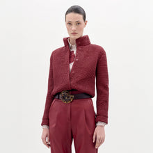 Load image into Gallery viewer, A woman stands against a plain background wearing the Zalta Jacket, a textured red jacket paired with a striped shirt, red pants, and a large black belt featuring an ornate buckle.
