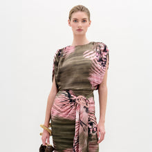 Load image into Gallery viewer, A woman stands against a plain background wearing the Alisa Blouse, featuring a pink and olive green pattern crafted from Italian fabric. She holds a brown bag and wears gold bracelets.
