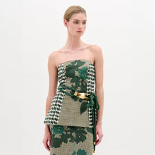 Load image into Gallery viewer, A woman wears the Astor Top, a strapless bustier in green, beige, and houndstooth Italian fabric with a matching skirt and a green belt with gold clasp, standing against a plain white background.

