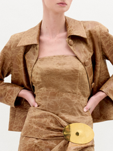 Load image into Gallery viewer, A woman wearing the Astor Top, a crinkled brown strapless style with a fitted waist and large gold belt buckle, stands against a plain white background.
