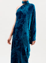 Load image into Gallery viewer, A person models the Anya Dress, a vibrant blue one-shoulder velvet design with a matching choker, single long sleeve, and patterned texture. The plain light background keeps the focus on the dress, with the person's face out of view.
