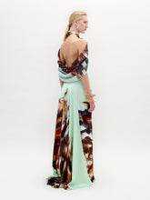Load image into Gallery viewer, A woman stands against a white background wearing the Carlina Dress, a floor-length light blue maxi made from Italian fabric with a brown and red feather-like pattern and a matching draped shoulder cape.
