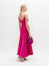 Load image into Gallery viewer, A woman poses against a white background in the Casiana Dress, a bright pink midi style made from Italian fabric with a deep V neckline. She pairs it with a matching small handbag and nude heels.
