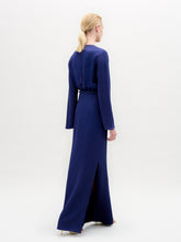 Load image into Gallery viewer, A person stands facing forward in the Cassy Dress—a long-sleeved, floor-length dark blue maxi with a keyhole neckline and black belt, crafted from luxurious Italian fabric—set against a plain white background.
