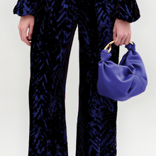Load image into Gallery viewer, A person stands against a plain background wearing the Como Pant in color eggplant velvet and the sofia bag small in color spectrum blue
