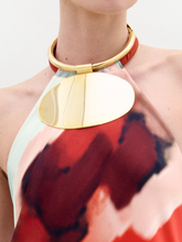 Load image into Gallery viewer, The Danielle Necklace features a gold-tone choker with a thick, round chain and a large flat oval pendant at the center, creating a minimalistic silhouette against a plain white background.
