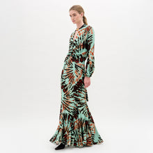 Load image into Gallery viewer, Against a plain white background, a person wears the Florina Skirt, crafted from luxurious Italian fabric. This long skirt showcases a vibrant tie-dye pattern with green, orange, and black hues cascading elegantly down its maxi length.
