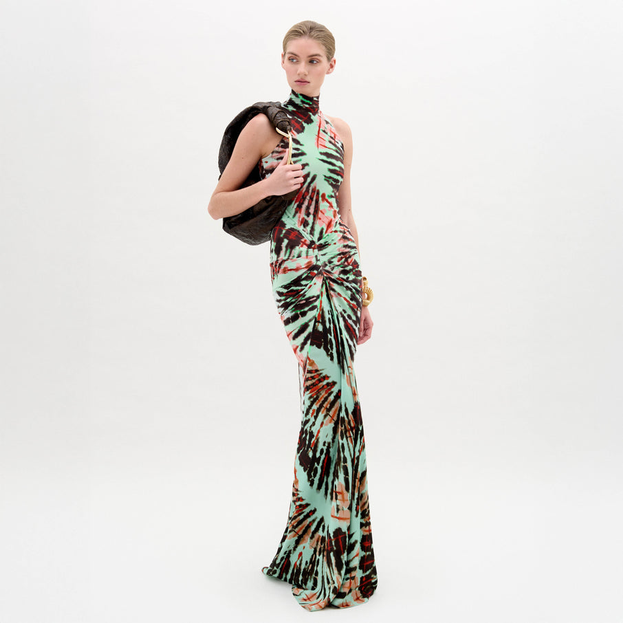 A woman wears the Frances Dress, a sleeveless, slim-fit maxi with a high neckline, holding a dark jacket over her shoulder against a plain white background.