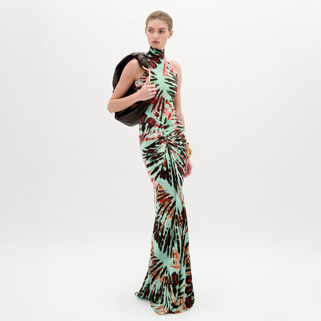 A woman wears the Frances Dress, a sleeveless, slim-fit maxi with a high neckline, holding a dark jacket over her shoulder against a plain white background.