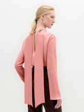 Load image into Gallery viewer, A woman stands against a plain background wearing the Gaby Blouse, a pink high-neck top with a front slit, paired with brown textured pants and a wide belt featuring a large gold oval buckle.
