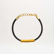 Load image into Gallery viewer, The Hadria Necklace is shown on a plain white background, featuring a black braided leather design with a gold clasp and gold embellishments.
