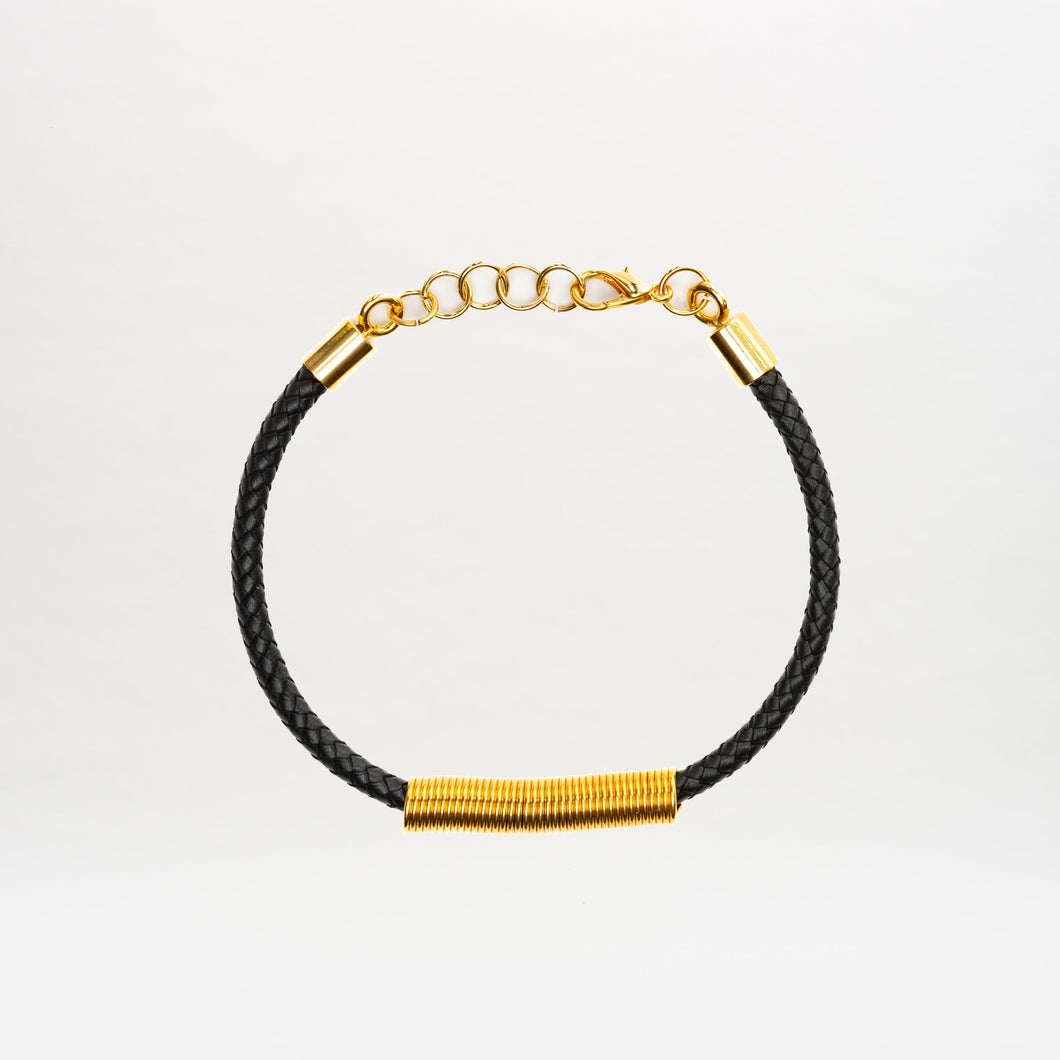 The Hadria Necklace is shown on a plain white background, featuring a black braided leather design with a gold clasp and gold embellishments.