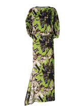 Load image into Gallery viewer, On August 19th, a woman poses against a light blue background wearing the Harriet Dress Floral Camo in green, black, and brown floral pattern. She is accessorized with high-heeled shoes and a bracelet.
