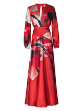 Load image into Gallery viewer, A person is wearing the Keira Dress in Pomegranate Abstract Flowers, featuring long sleeves and a floral print, standing against a plain blue background as if ready for the upcoming events on August 19th.
