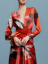 Load image into Gallery viewer, A person is wearing the Keira Dress in Pomegranate Abstract Flowers, featuring long sleeves and a floral print, standing against a plain blue background as if ready for the upcoming events on August 19th.
