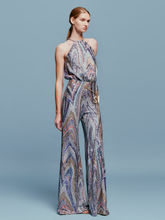 Load image into Gallery viewer, Against a plain blue background, a person stands poised in the Lauretta Jumpsuit Sequin Waves, featuring a sleeveless, high-neck design with a colorful, swirling pattern. The outfit showcases wide-leg pants and comes with a belt—perfectly capturing the style for upcoming events between August 19th and September 2nd, 2024.
