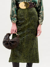 Load image into Gallery viewer, Person wearing a green patterned skirt and holding a brown bag on a white background
