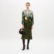 Load image into Gallery viewer, Woman wearing a green patterned top and green skirt with black knee-high boots on a white background
