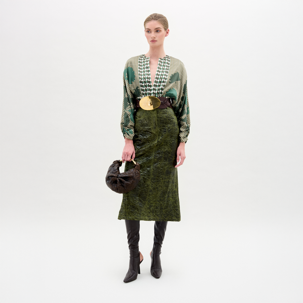 Woman wearing a green patterned top and green skirt with black knee-high boots on a white background