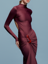 Load image into Gallery viewer, A person in a fitted, long-sleeve Lena Dress Burgundy with a high neckline stands against a plain blue background. The gown, perfect for an August 19th, 2024 gala, features elegant draping and a red embellishment near the waist.
