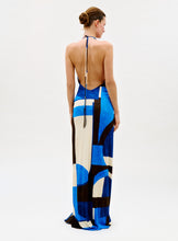 Load image into Gallery viewer, A woman faces away, wearing the Malek Dress—a backless, halter-neck style featuring a bold geometric pattern in blue, black, and white. Her hair is styled in a neat bun against a plain white background.

