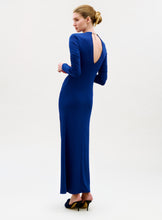 Load image into Gallery viewer, Woman in a long, fitted Mara Dress with long sleeves and an open back, shown in profile wearing high heels and her blonde hair styled in a low bun.
