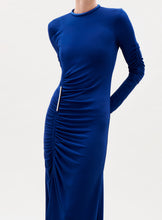 Load image into Gallery viewer, A person in the Mara Dress—a long-sleeved, royal blue dress with a fitted silhouette, high neckline, and ruching along the side and front—stands against a plain light background. The person's face is not visible.
