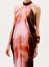 Load image into Gallery viewer, Someone wearing the Mene Dress, a flowing halter-neck piece with a pink and brown gradient, styled with a chunky dark choker and matching statement bracelet, set against a plain white background.
