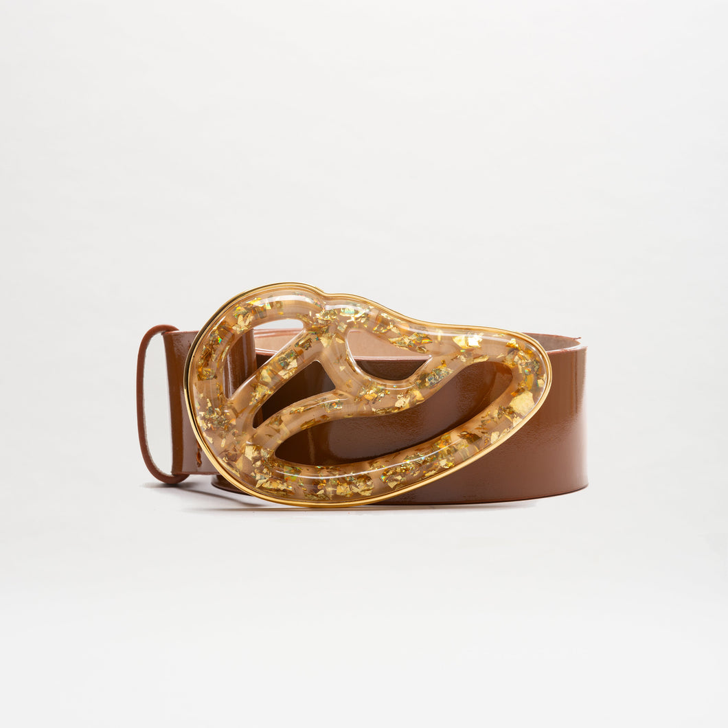 The Nala Belt is a wide brown Italian leather belt with a large, abstract Petralux buckle accented by embedded gold flakes. Made in Colombia, it’s displayed against a plain white background.