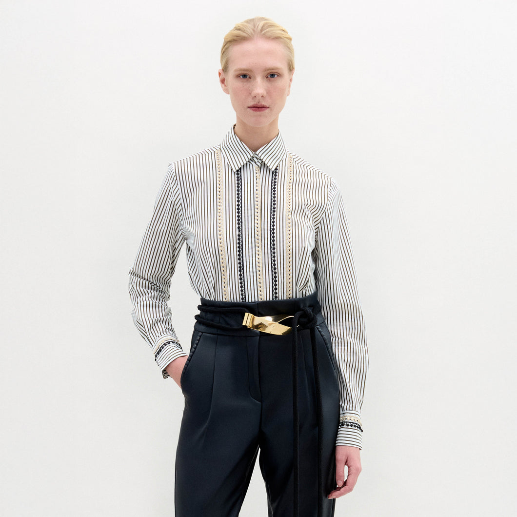 Person stands against a plain background, wearing the Naroa Blouse— a striped 100% cotton button-up— tucked into high-waisted black pants with a gold-buckle belt.