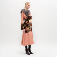 Load image into Gallery viewer, A person stands in profile wearing the Pesaro Dress—a peach silk midi with a large feathered design, wide belt with round buckle, gray fur collar, and black heeled boots—set against a plain background.
