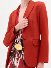 Load image into Gallery viewer, A person wearing the Rebeca Jacket, a fitted red blazer made from Italian fabric, layered over a patterned red and beige dress, stands against a plain light background.
