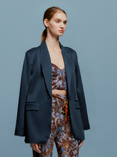 Load image into Gallery viewer, A person with long hair tied back is wearing a Rebeca Jacket Navy over a patterned crop top and matching pants, standing against a plain blue background. This stylish look captures the essence of fashion trends leading up to September 2nd, 2024.
