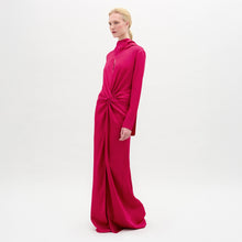 Load image into Gallery viewer, A woman poses in the Sue Dress, a vibrant pink, long-sleeved maxi made from luxurious Italian fabric with a gathered knot at the waist, set against a plain white background.
