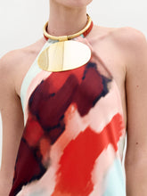 Load image into Gallery viewer, A woman poses against a white background wearing the Zeffa Dress, a sleeveless, floor-length silk maxi with an abstract red, aqua, and white pattern, paired with gold jewelry.
