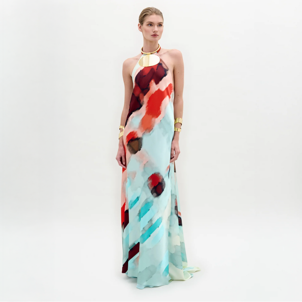 A woman poses against a white background wearing the Zeffa Dress, a sleeveless, floor-length silk maxi with an abstract red, aqua, and white pattern, paired with gold jewelry.